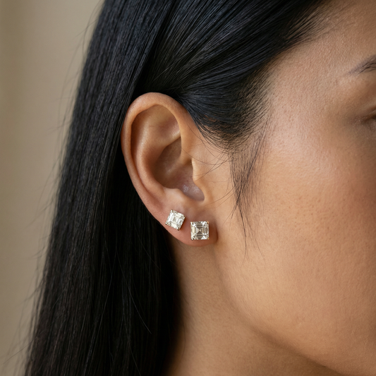 Close-up of a person wearing diamond stud earrings with a neutral background
