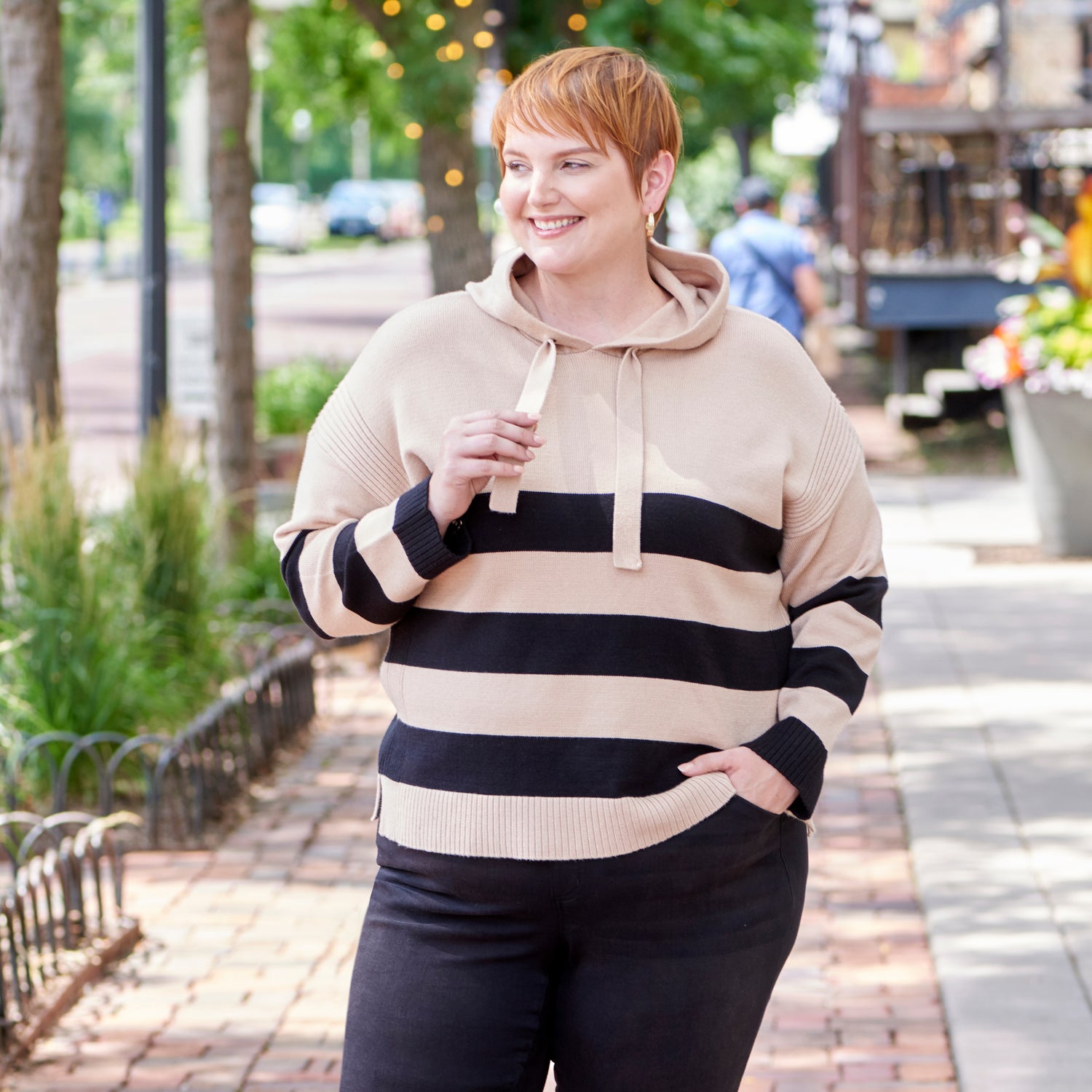 Woman wearing a striped hoodie and black pants walking on a sidewalk.