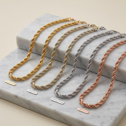 Three braided necklaces in gold, silver, and rose gold on a marble surface.