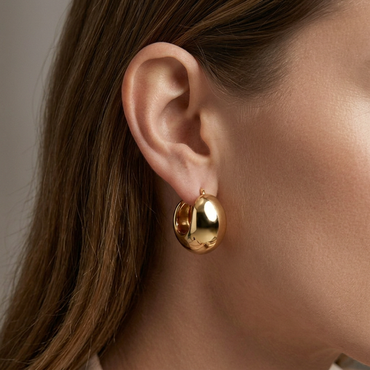 A close-up of a model's ear wearing a polished gold huggie hoop earring.